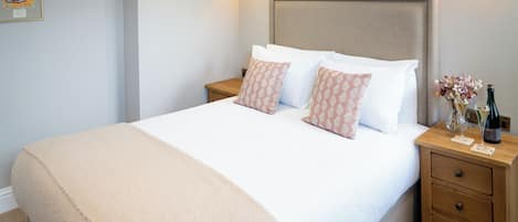 A neatly made bed with a beige blanket, two bedside tables with lamps, and a framed picture on the wall.