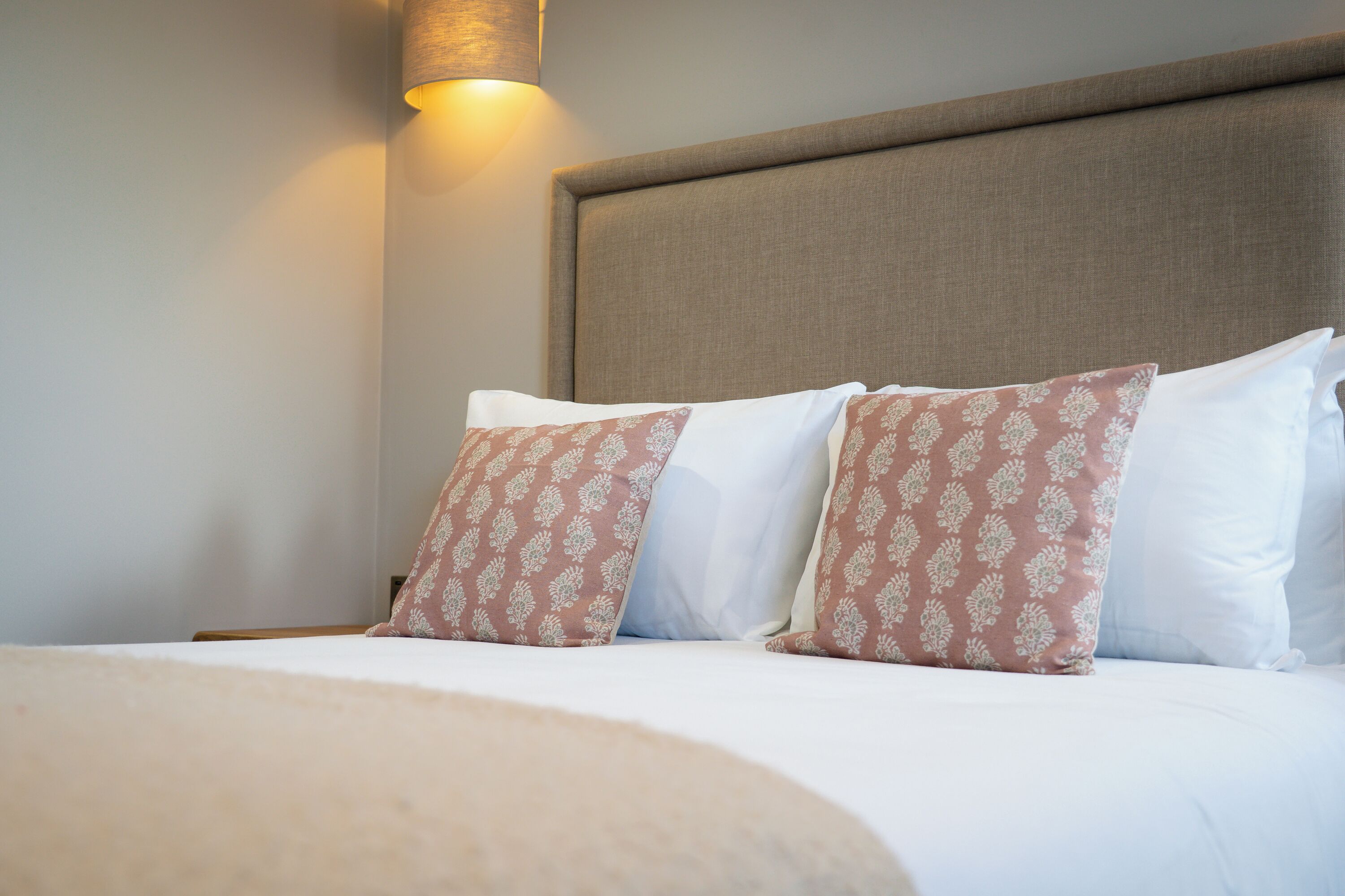 A neatly made bed with patterned pillows, a headboard, and a wall-mounted light fixture.