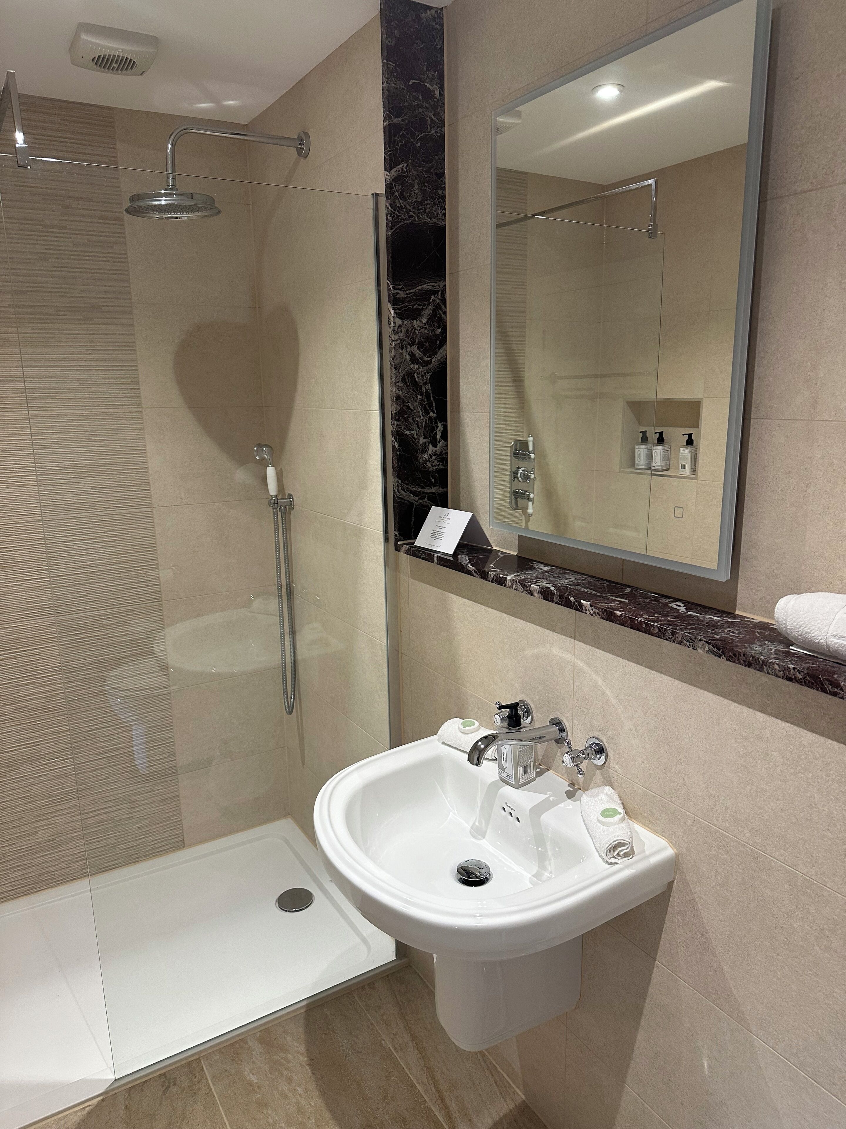 A modern bathroom with a glass-enclosed shower, a white sink with a mirror above, and a marble accent wall.