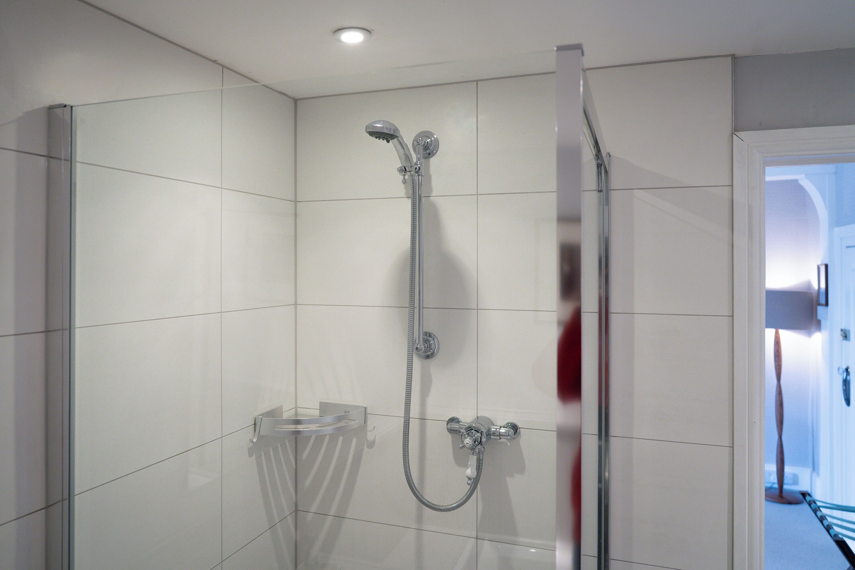 Un baño moderno con cabina de ducha de vidrio, un inodoro y una puerta visible que da a otra habitación.