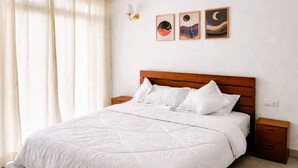 A bedroom with a wooden headboard, white bedding, a nightstand, and three wall-mounted artworks.