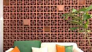 A green sofa with orange and white cushions, a decorative wall with geometric patterns, and a plant.