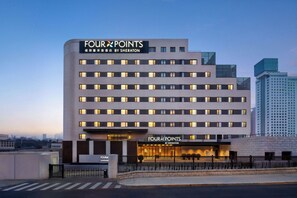 Een meerhoog hotel met een opvallend 'Four Points by Sheraton'-bord, een modern architectuurontwerp en een goed verlichte entree.