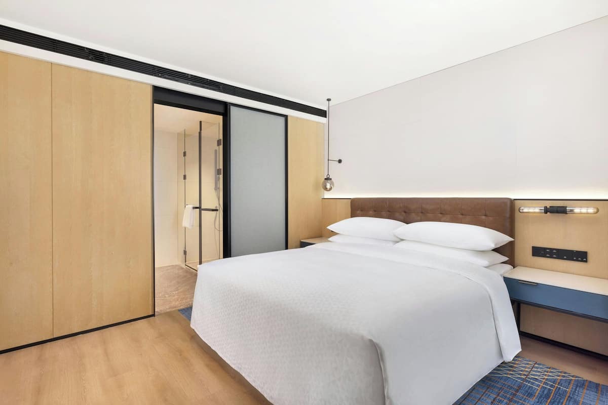 A hotel room with a bed, a nightstand, a wall-mounted light, and a sliding door closet.