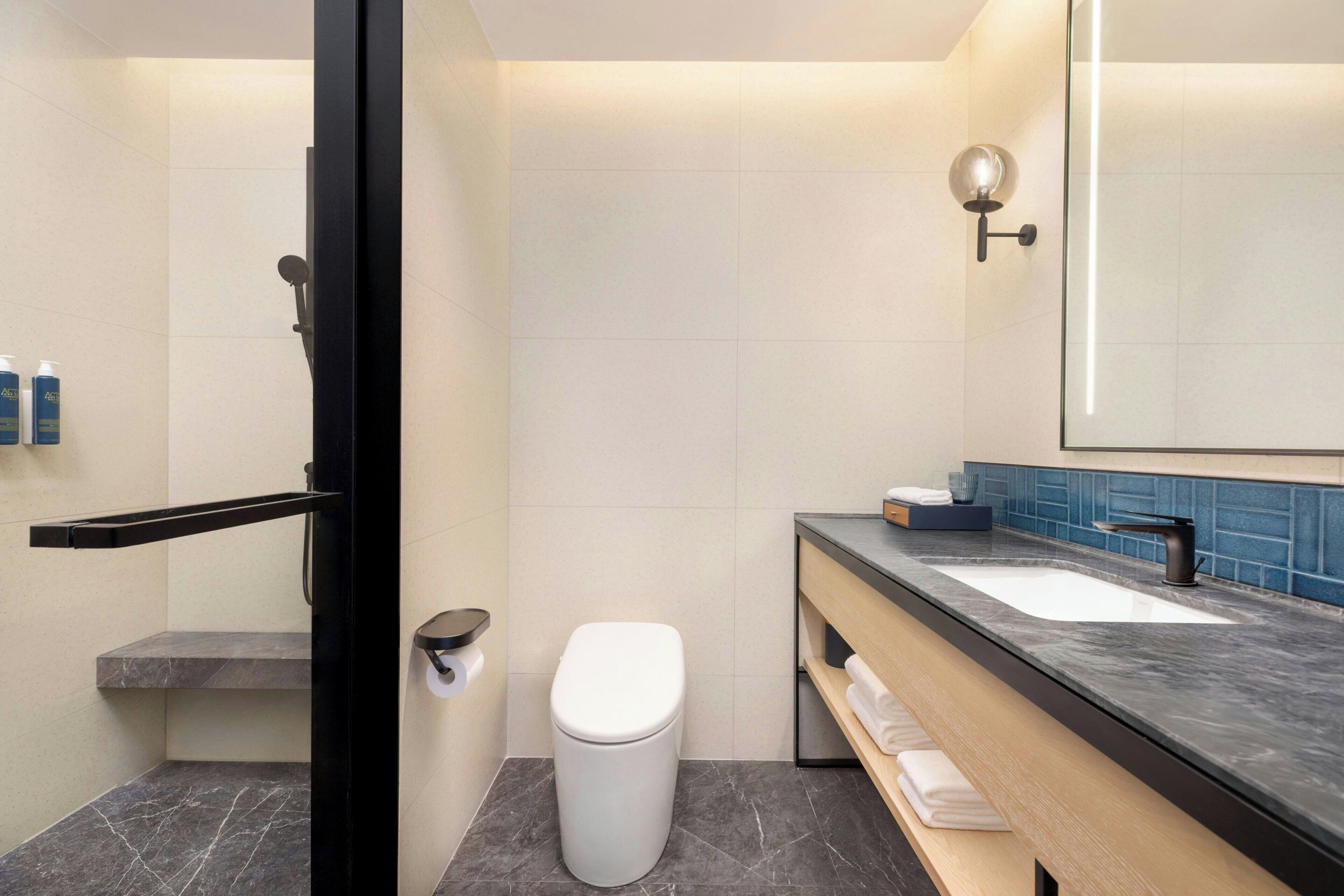 Un baño moderno con inodoro blanco, lavamanos con encimera negra y espejo con luz empotrada.