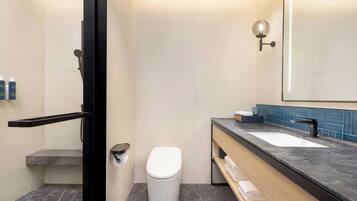 Un baño moderno con inodoro blanco, lavamanos con encimera negra y espejo con luz empotrada.