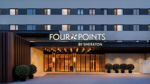 Een hotelingang met een moderne gevel, grote ramen en een bord waarop 'FOUR POINTS BY SHERATON' staat.
