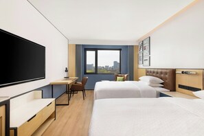 Hotelkamer met groot bed, bureau, stoel, televisie en raam met uitzicht over de stad.