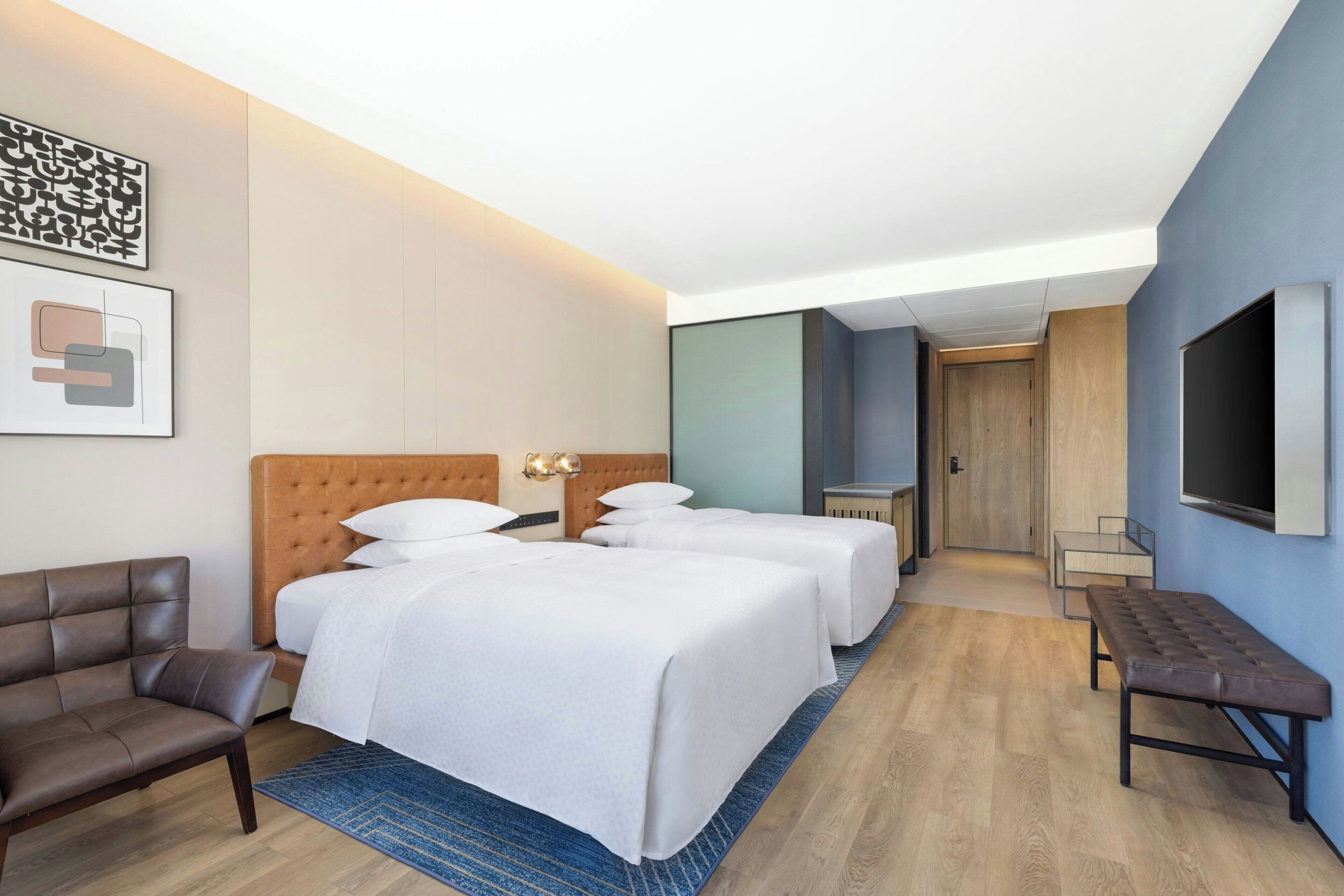 A hotel room with a large bed, a sofa, a bench, and a TV on the wall.