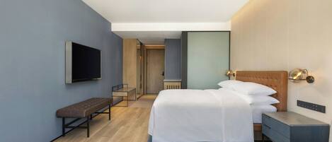 Una habitación de hotel moderna con cama, banco, mesita de noche y televisor de pantalla plana.