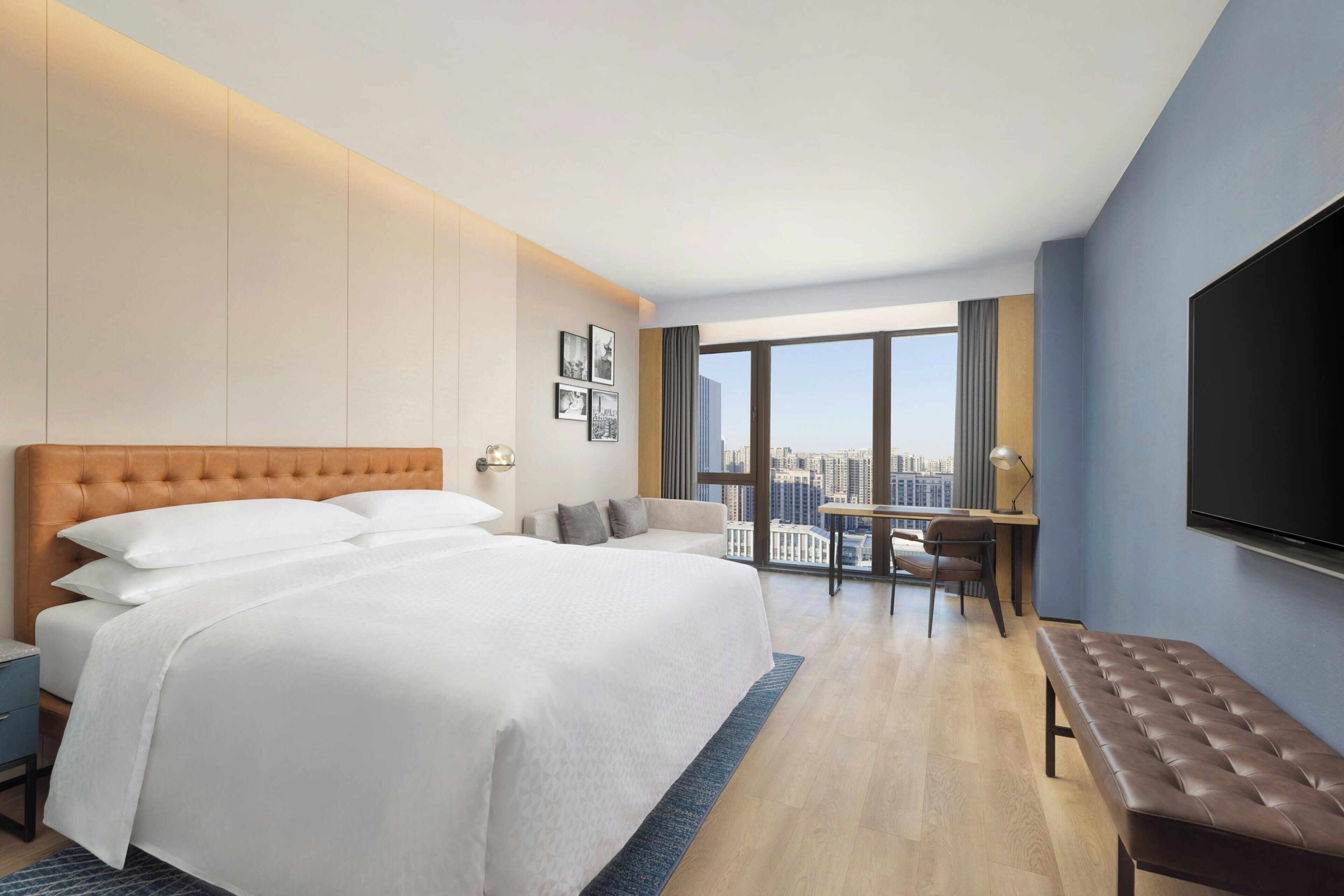 Una habitación de hotel con una cama grande, un escritorio, una silla, un banco y un televisor.