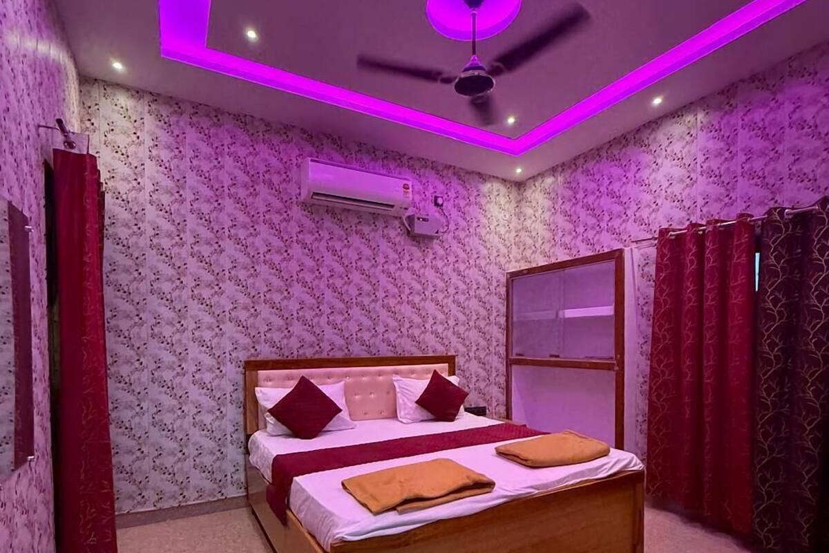 Een slaapkamer met een bed, een plafondventilator, een airconditioner en behang met een patroon.