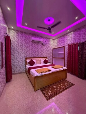 A bedroom with a bed, a ceiling fan, an air conditioning unit, and patterned wallpaper. - Hotel Vijaya Palace (Ayodhya)
