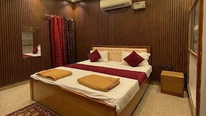 A modern bedroom with a wooden bed, a ceiling fan, an air conditioning unit, and a bedside table. - Hotel Vijaya Palace (Ayodhya)