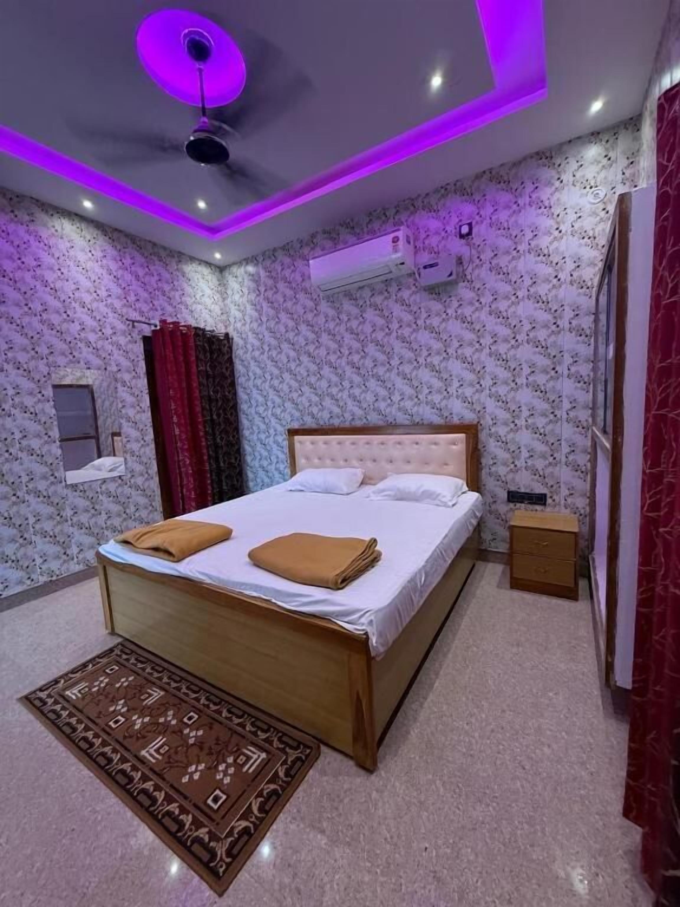A bedroom with a bed, a nightstand, a ceiling fan, and patterned wallpaper.