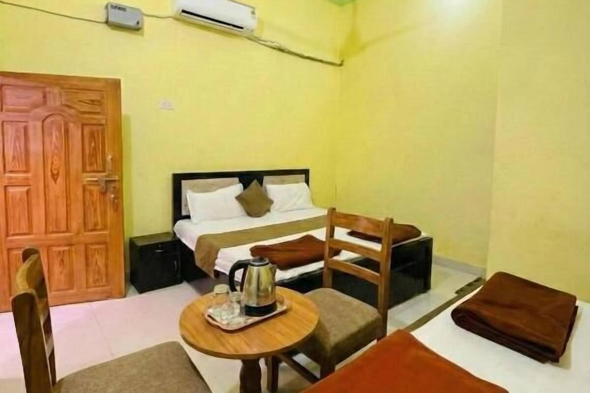 Een kamer met een bed, een tafel met waterkoker, een stoel en een opgevouwen deken.