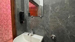 A bathroom with a white sink, a mirror, and a marble wall. - Hotel Vijaya Palace (Ayodhya)