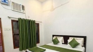 A bedroom with a bed, green curtains, a ceiling fan, and an air conditioning unit. - Hotel Vijaya Palace (Ayodhya)