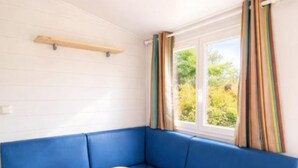 A room with a blue sofa, a wooden table, and a window with curtains. - COTTAGE PARKS Terrasses du Lac - Mobile home 5 persons lake view (Pont-de-Salars)