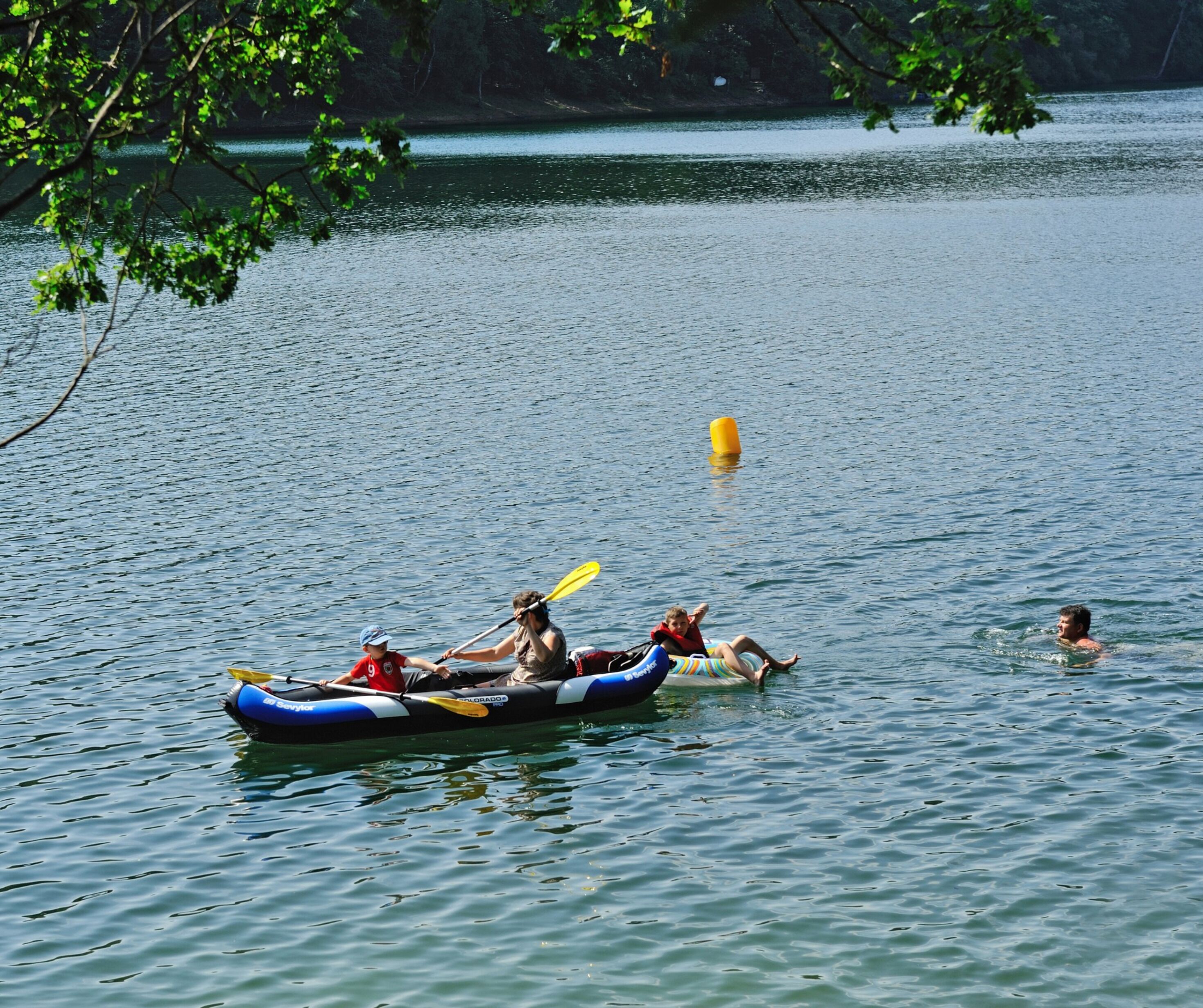 A calm lake with a group of people in a blue and white inflatable raft, paddling.