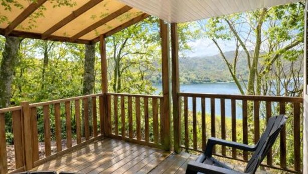 A covered deck with wooden railings, a bench, and chairs, overlooking a lake surrounded by trees. - COTTAGE PARKS Terrasses du Lac - Mobile home 5 persons lake view (Pont-de-Salars)