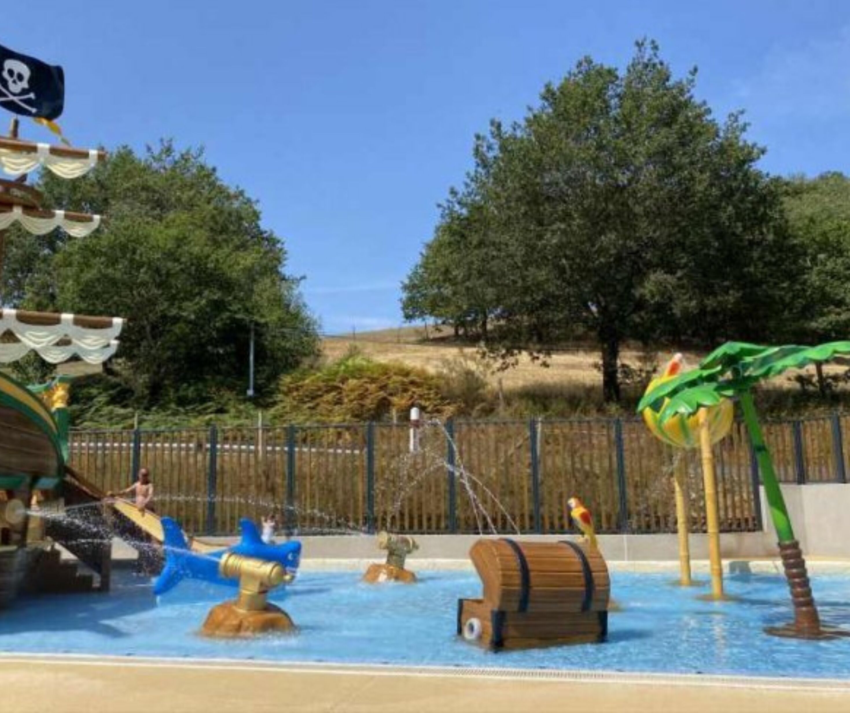 A water play area with pirate-themed structures, including a ship, a barrel, and a pirate flag.