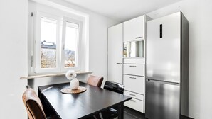 Ett modernt kök med ett kylskåp i rostfritt stål, vita köksskåp och en matplats med ett bord och stolar.