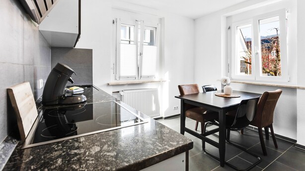 Ett modernt kök med en inbyggd spis, ett matbord med stolar och stora fönster som ger utsikt över omgivningen.