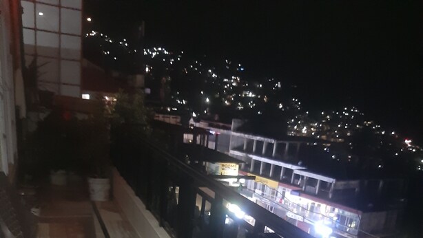 A balcony with chairs, a railing, and a view of a cityscape at night. - Marvelous 2-bedroom house in Solan perfect for a relaxing getaway (Solan)