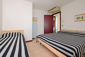 Une pièce avec deux lits, une porte, un radiateur et un tableau au mur.