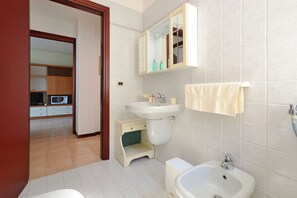 Une salle de bain avec un lavabo, un miroir et des toilettes. Il y a un petit meuble sous le lavabo et une serviette accrochée au mur.