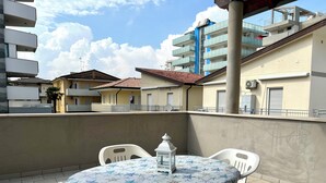 Una terraza en la azotea con una mesa redonda y sillas, un farol decorativo y vistas de edificios residenciales.
