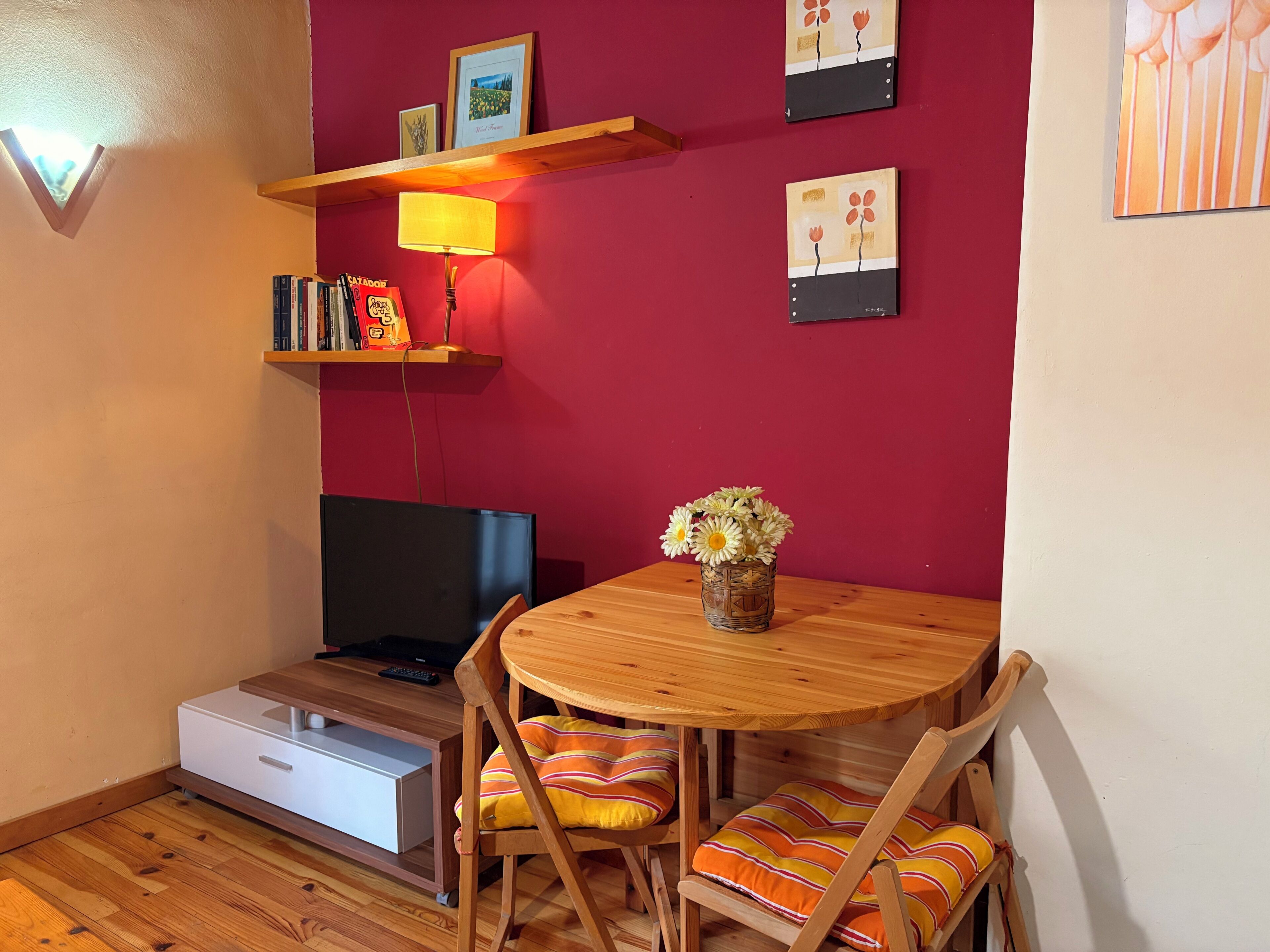 A cozy room with a TV, wooden furniture, a lamp, and artwork on the wall.