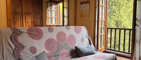 A cozy room with a patterned sofa, wooden furniture, and a view of greenery through a window.