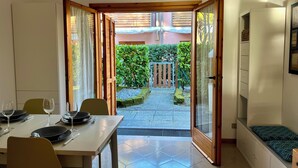 Un comedor con una mesa preparada para dos, un reloj en la pared y vistas a un jardín a través de una puerta abierta.