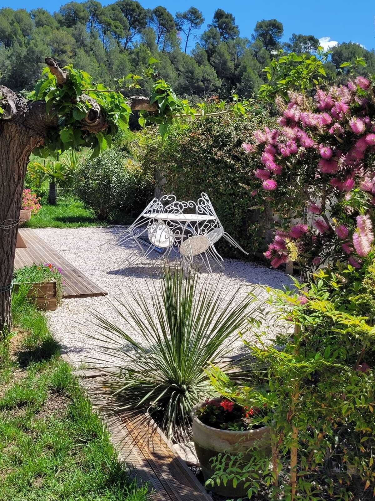 Un jardin avec une chaise en métal, une terrasse en bois et diverses plantes.