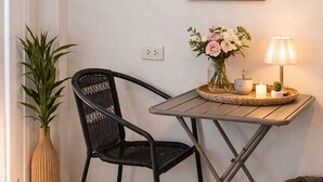A corner room with a black woven chair, a small table with a lamp, a vase of flowers, and a framed botanical print on the wall. - Blissful well treat (Ko Pha-ngan)