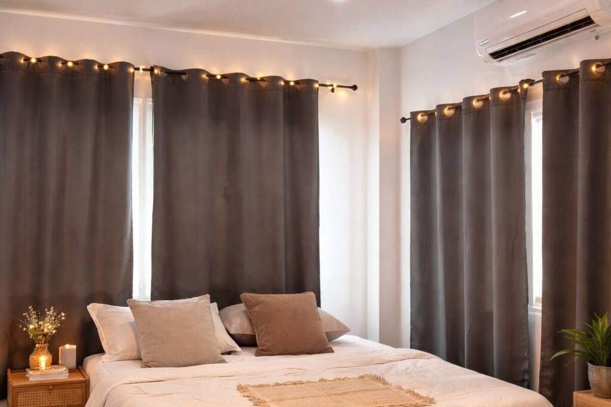 Een slaapkamer met een bed, gordijnen, een nachtkastje, een plant en een airconditioning.
