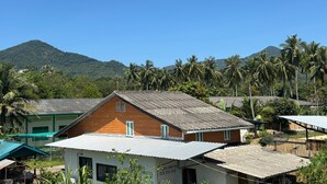 A residential area with houses, a mountain in the background, and palm trees. - Blissful well treat (Ko Pha-ngan)