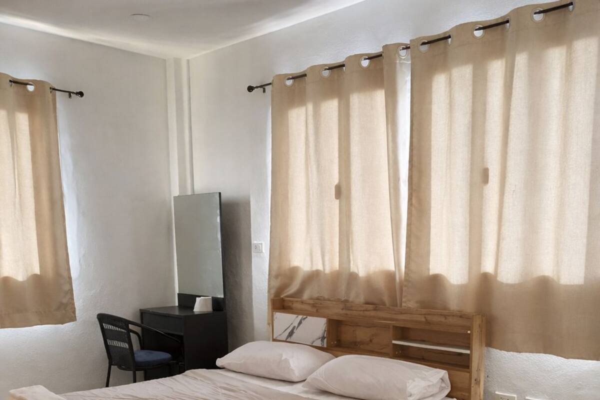 Een slaapkamer met een houten bed, een bureau, een stoel, een spiegel en beige gordijnen.