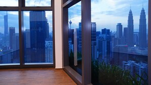 A room with large windows overlooking a cityscape, featuring modern buildings and a view of the skyline. - Luxury One Bedroom Apartment with KLCC View by JD Hospitality (Kuala Lumpur)