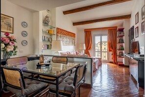 A dining area with a glass table and chairs, a kitchen area with a stove, and a living space with a sofa and a window. - Arno Dream by MMega Homes and Villas (Florence)