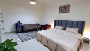 Ein Schlafzimmer mit Bett, Nachttisch, Schlafsofa, kleinem Tisch, Pflanze und Wandbild.