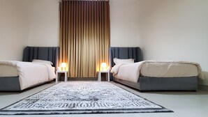 Ein Doppelzimmer mit zwei Betten, einem gemusterten Teppich und einem senkrechten Vorhang.