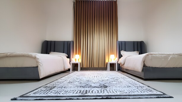 Ein Hotelzimmer mit zwei Betten, einem gemusterten Teppich und einem senkrechten Vorhang.