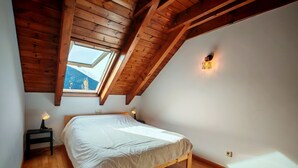 Een slaapkamer met een houten plafond, dakraam, een bed, nachtlampen en uitzicht op bergen.