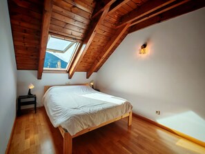 Un dormitorio con techo de madera, tragaluz, cama, lámparas de noche y vistas a las montañas.