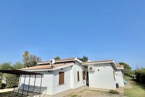 Ein eingeschossiges Gebäude mit Ziegeldach, überdachter Terrasse und kleinem Garten.