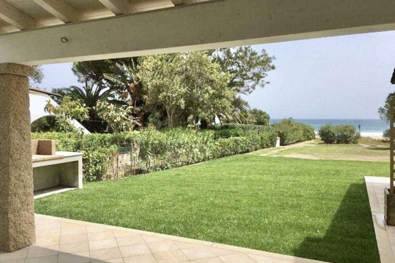 Ein überdachter Patio-Bereich mit Meerblick, einem gepflegten Rasen und einer Steinsäule.