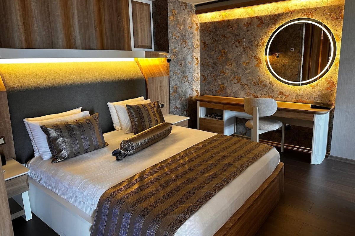 Ein modernes Schlafzimmer mit Bett, Nachttisch, Schreibtisch, Stuhl und einem runden Spiegel.